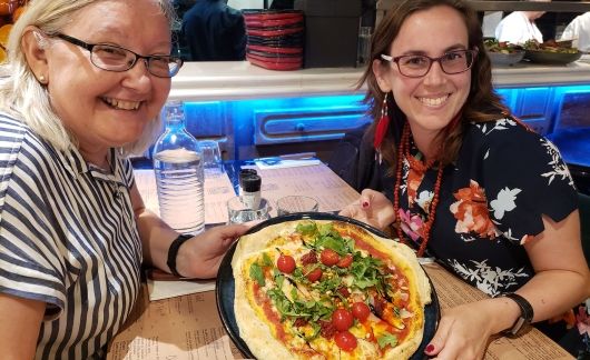 Two women in Toulouse holding up a pizza in a cafe